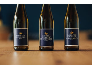 Riesling, Grauburgunder und Weißburgunder Flaschen auf Tisch vor dunklem Hintergrund