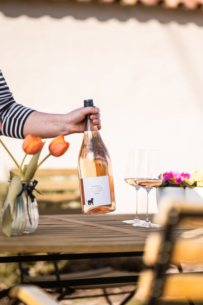 Little Lion Rosé Magnum wird mit Hand auf Tisch mit Blumen und Gläser gestellt
